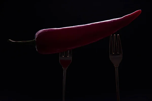 Hot red pepper is put on two forks on a black background.