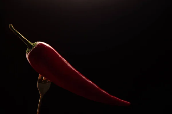 Ripe red pepper is put on the tip of the fork on a black background.