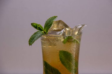 Hafif bir arka plan üzerinde buz ve nane yaprakları ile bir bardağa dökülen hafif ferahlatıcı içecek.