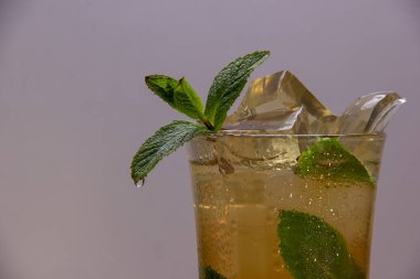 Hafif bir arka plan üzerinde buz ve nane yaprakları ile bir bardağa dökülen hafif ferahlatıcı içecek.