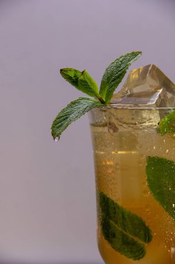 Hafif bir arka plan üzerinde buz ve nane yaprakları ile bir bardağa dökülen hafif ferahlatıcı içecek.