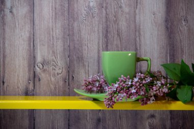 Bir tabak ile yeşil bir fincan sarı rafta, yanında çiçek lila bir dalı, ahşap bir arka plan üzerinde tüm öğeleri.