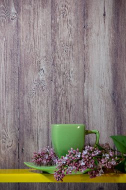 Bir tabak ile yeşil bir fincan sarı rafta, yanında çiçek lila bir dalı, ahşap bir arka plan üzerinde tüm öğeleri.