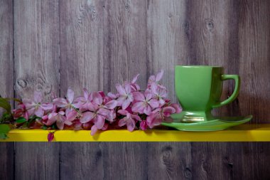 Yeşil fincan, tabak, sarı rafta sakura çiçek açan dal, ahşap bir arka plan arkasında.