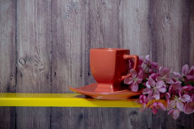 Kırmızı fincan, tabak, sarı rafta sakura çiçek açan dal, ahşap bir arka plan arkasında.