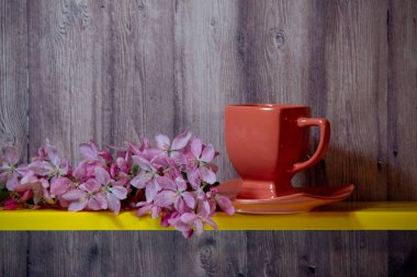 Kırmızı fincan, tabak, sarı rafta sakura çiçek açan dal, ahşap bir arka plan arkasında.