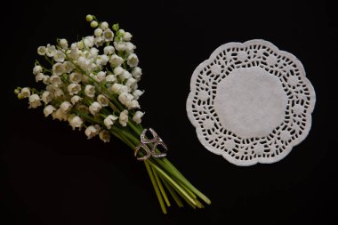 Broş ile vadinin zambak bir buket, açık çalışma yuvarlak kağıt peçete siyah bir arka plan üzerinde yalan.