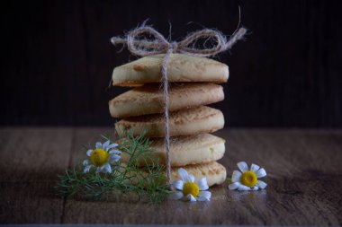 Beş yuvarlak kurabiye bir ip, üç papatya, ahşap bir arka plan üzerinde çim bir dalı ile bir yay ile dekore.