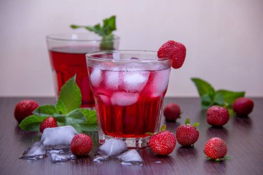 İki bardak buz ile kırmızı bir kokteyl döktü, sonraki olgun çilek, nane ve buz küpleri bir dalı.