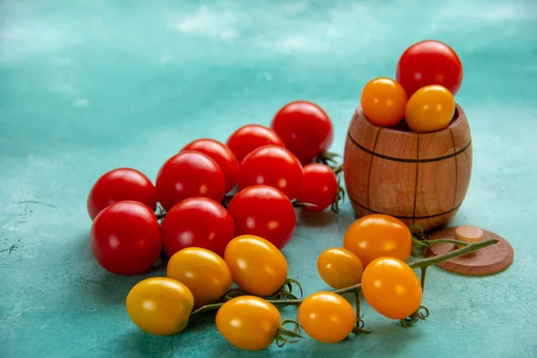A branch of red tomato cherry, a branch of yellow cherry tomatoes, ripe tomatoes in a small wooden barrel on a blue background.