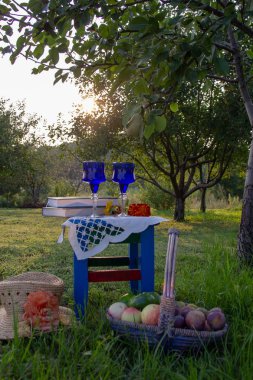 İki cam mavi gözlük, iki kitap, bir elma ve çiçekler bir tabure üzerinde bir masa örtüsü ile süslenmiş standı, bir yaz bahçesi ve olgun bir armut ile bir ağaç etrafında.