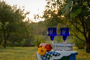 İki cam mavi gözlük, iki kitap, bir elma ve çiçekler bir tabure üzerinde bir masa örtüsü ile süslenmiş standı, bir yaz bahçesi ve olgun bir armut ile bir ağaç etrafında.