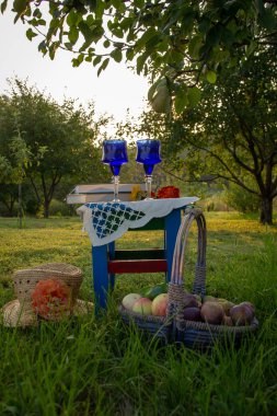 İki cam mavi gözlük, iki kitap ve çiçek bir tabure üzerinde bir masa örtüsü, elma ve erik ile bir sepet ile süslenmiş, bir hasır şapka bir ağaç üzerinde olgun bir armut ile bir yaz bahçesinde yer almaktadır.