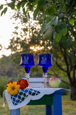 İki cam mavi gözlük, iki kitap, bir elma ve çiçekler bir tabure üzerinde bir masa örtüsü ile süslenmiş standı, bir yaz bahçesi ve olgun bir armut ile bir ağaç etrafında.