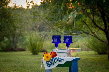 İki cam mavi gözlük, iki kitap, bir elma ve çiçekler bir tabure üzerinde bir masa örtüsü ile süslenmiş standı, bir yaz bahçesi ve olgun bir armut ile bir ağaç etrafında.