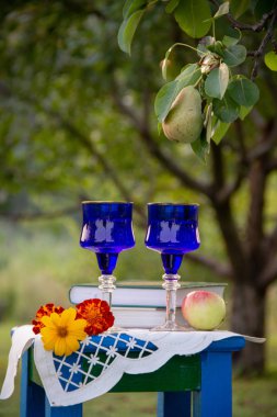 İki cam mavi gözlük, iki kitap, bir elma ve bir tabure üzerinde bir masa örtüsü ile süslenmiş çiçekler bir ağaç üzerinde olgun bir armut ile bir yaz bahçesinde yer almaktadır.