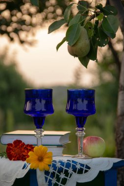 İki cam mavi gözlük, iki kitap, bir elma ve bir tabure üzerinde bir masa örtüsü ile süslenmiş çiçekler bir ağaç üzerinde olgun bir armut ile bir yaz bahçesinde yer almaktadır.