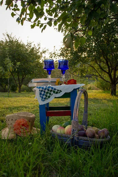 İki cam mavi gözlük, iki kitap ve çiçek bir tabure üzerinde bir masa örtüsü, elma ve erik ile bir sepet ile süslenmiş, bir hasır şapka bir ağaç üzerinde olgun bir armut ile bir yaz bahçesinde yer almaktadır.