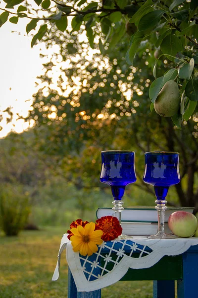 İki cam mavi gözlük, iki kitap, bir elma ve çiçekler bir tabure üzerinde bir masa örtüsü ile süslenmiş standı, bir yaz bahçesi ve olgun bir armut ile bir ağaç etrafında.