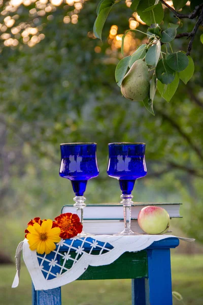 İki cam mavi gözlük, iki kitap, bir elma ve çiçekler bir tabure üzerinde bir masa örtüsü ile süslenmiş standı, bir yaz bahçesi ve olgun bir armut ile bir ağaç etrafında.