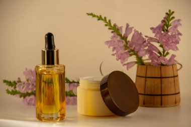 Bir damlalık ile cam şişede Doğal yüz yağı, yüz kremi için ambalaj, beyaz bir arka plan üzerinde ahşap bir varil çiçek bir buket.