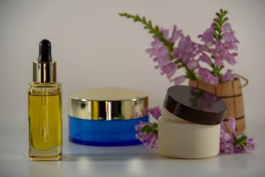 Bir pipet ve doğal yüz yağı ile Cam kavanoz, yüz kremi ile iki paket, beyaz bir arka plan üzerinde çiçek kokulu bir buket ile ahşap bir varil.