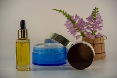 Bir pipet ve doğal yüz yağı ile Cam kavanoz, yüz kremi ile iki paket, beyaz bir arka plan üzerinde çiçek kokulu bir buket ile ahşap bir varil.