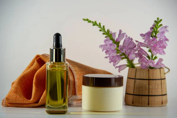 Natural face oil in a glass vial with a dropper, face cream, a bouquet of flowers in a wooden barrel, a piece of orange natural tissue on a white background.