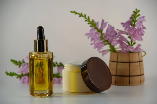 Natural face oil in a glass vial, face cream, a bouquet of flowers in a wooden barrel on a white background.