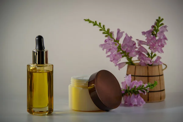 Natural face oil in a glass bottle with a dropper, packaging for face cream, a bouquet of flowers in a wooden barrel on a white background.