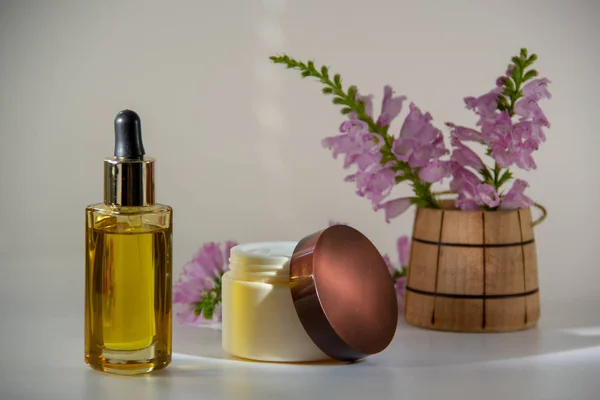 Gold natural face oil in a glass bottle with a dropper, packaging for face cream, a fragrant bouquet of flowers in a wooden barrel on a white background.