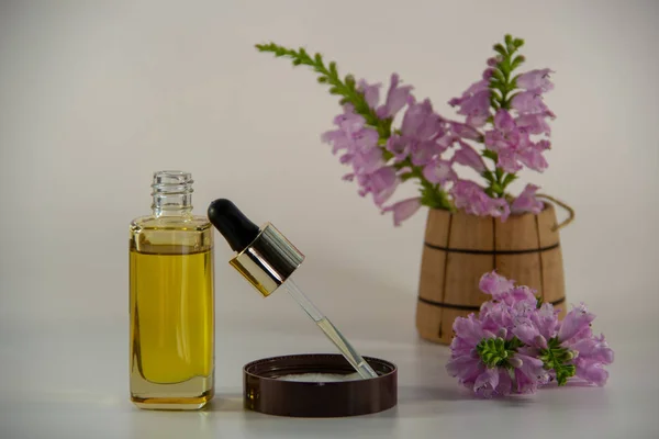 Natural face oil with a glass bottle, a glass dropper, cream covers, a wooden vase with a bouquet of flowers on a white background.