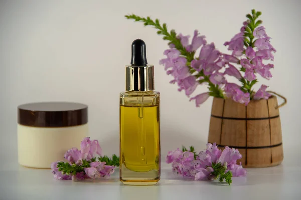 Glass bottle with golden natural face oil and a dropper, packaging for face cream, a fragrant bouquet of purple flowers in a wooden barrel on a white background.