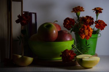 Yeşil bir tabakta olgun elma natürmort, küçük bir dekoratif kova içinde kadife bir buket, kitaplar, beyaz bir arka plan üzerinde bir gülümseme şeklinde bir şiş ile elma yarıya.
