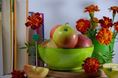 Yeşil bir tabakta olgun elma natürmort, küçük bir dekoratif kova içinde kadife bir buket, kitaplar, beyaz bir arka plan üzerinde bir gülümseme şeklinde bir şiş ile elma yarıya.