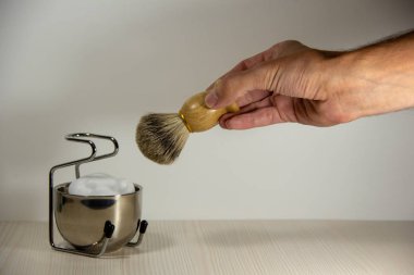 Bir erkek el bir fırça ile ahşap bir tıraş jilet tutar, bir stand üzerinde köpük ile metal bir kase yanında. Tıraş aksesuarları. Açık arka plan.