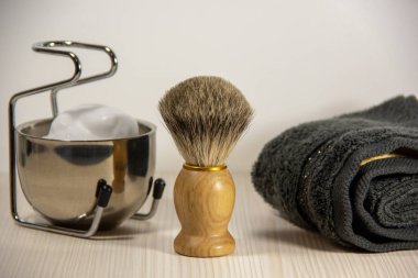 Tıraş aksesuarları: fırçaile ahşap bir tıraş jilet, bir stand üzerinde köpük ile metal bir kase, gri bir havlu. Açık arka plan.
