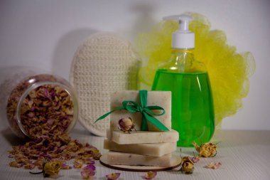 El yapımı doğal sabun fiyonkla süslenmiş, kavanozda kurumuş gül yaprakları, şişede sıvı sabun, vücut için iki bez. Banyo aksesuarları.