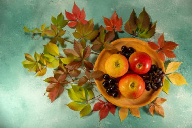 Tahta bir tabakta olgun üzüm ve elmalar. Parlak sonbahar yapraklı bir üzüm dalı. Sonbahar sakin bir hayat.