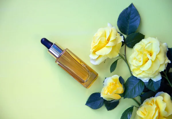 Nature cosmetics in glass bottle with a pipette and yellow roses. Serum with herbal extracts for skincare. The concept of health and beauty. Flat lay, copy space.