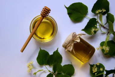 Ballı cam kavanoz, yuvarlak cam bir tabak, bal için yuvarlak bir tahta sopa, çiçek açan bir ıhlamur dalı. Vitamin konsepti, doğal tatlılar. Düz yat, boşluğu kopyala.