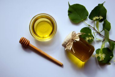 Ballı cam kavanoz, yuvarlak cam bir tabak, bal için yuvarlak bir tahta sopa, çiçek açan bir ıhlamur dalı. Vitamin konsepti, doğal tatlılar. Düz yat, boşluğu kopyala.