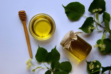 Ballı cam kavanoz, yuvarlak cam bir tabak, bal için yuvarlak bir tahta sopa, çiçek açan bir ıhlamur dalı. Vitamin konsepti, doğal tatlılar. Düz yat, boşluğu kopyala.