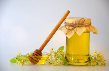 Lezzetli ballı cam bir kavanoz, bal için yuvarlak bir tahta sopa, kokulu ıhlamur çiçekleri. Sağlıklı gıda konsepti. Yatay görünüm, alanı kopyala.