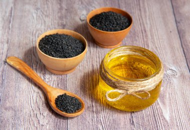 Cam kavanoz susam yağı ve tahta bir kase içinde çiğ siyah susam tohumu ve tahta bir arka planda kaşık. Faydalı doğal yağ. Doğal ve sağlıklı gıda konsepti.