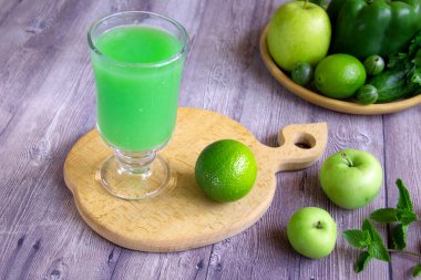 Meyve, sebze ve sebzelerden yapılmış yeşil meyve püresi. Bir bardak vejetaryen içeceği, elma, limon, salatalık, dolma biber, bektaşi üzümü, nane, ahşap arka planda maydanoz. Detoks ve diyet gıda konsepti.
