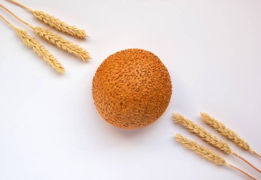 Susamlı ya da keten tohumu ve buğday kulaklı yuvarlak ekmek. Taze kabuklu ekmek ve beyaz arka planda olgun buğday kulakları. Sağlıklı gıda konsepti. Fırın ürün etiketi için tasarım ögesi. Boşluğu kopyala.