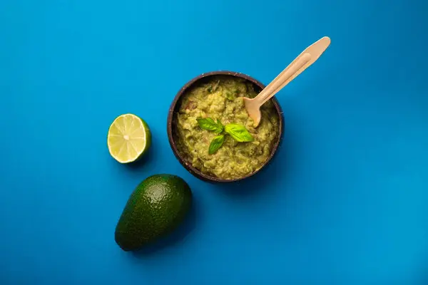 Mavi bir arka plan üzerinde malzemelerle Guacamole kase. Üstte görüntü