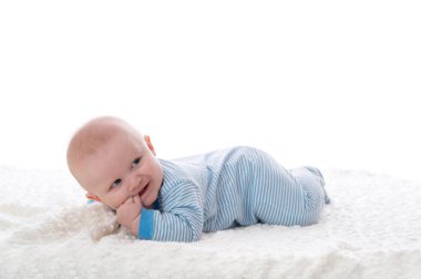 Beyaz bir battaniye karnına yatan 2 aylık erkek bir bebek. O pijama giyiyor, parmaklarını ağzına ve muzip bir gülümseme vardır. Beyaz bir arka plan üzerinde stüdyoda vurdu.