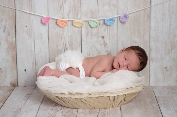 木製のボウルに眠っている古い 週新生児の女の子 木製の背景にあるパステル色 ハート形のガーランド — ストック写真